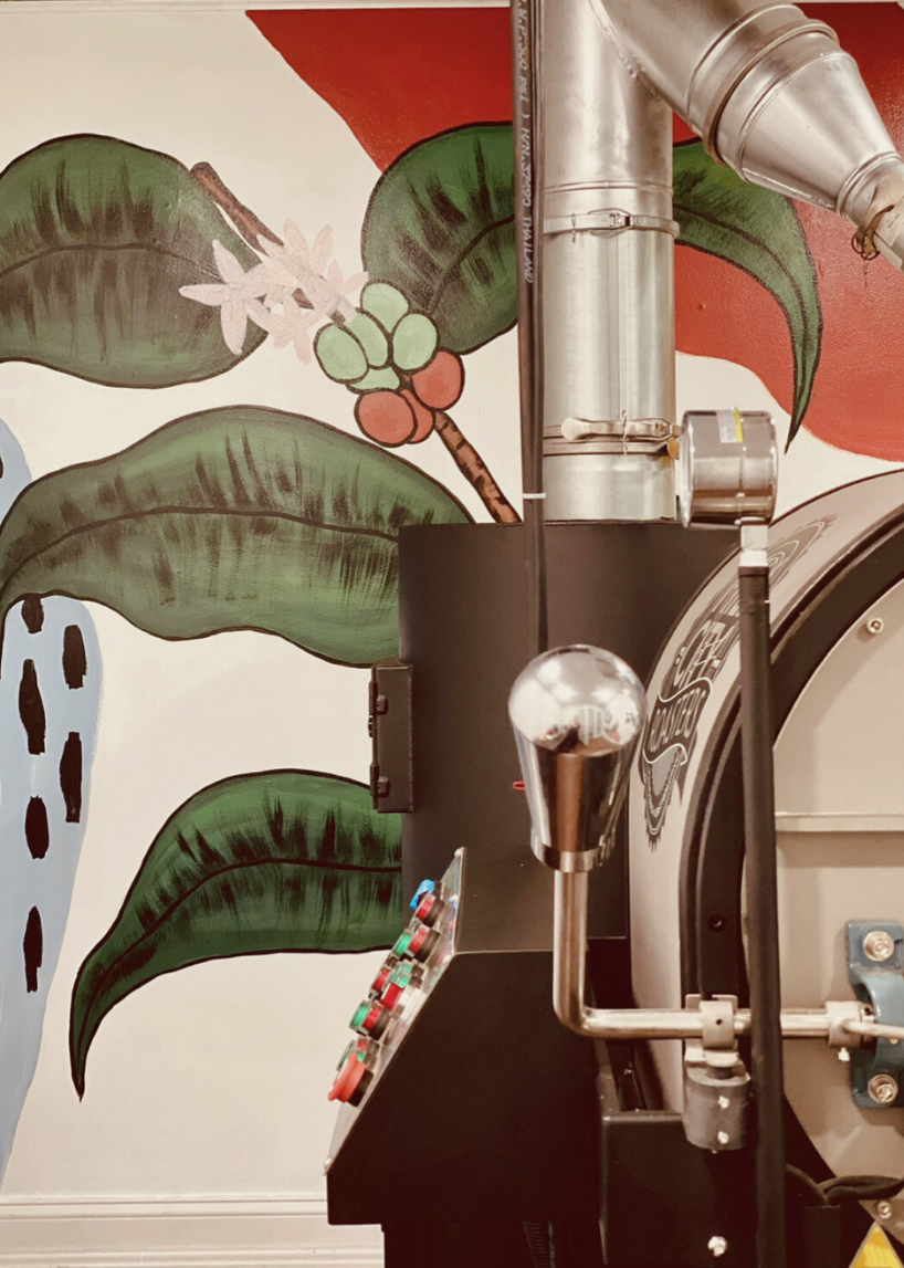 The Live Oak coffee roaster in front of a hand-painted coffee plant mural